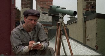 Movie still from “The Brink's Job” (1978), directed by William Friedkin – A man sitting next to a telescope looking at his cell phone; Medium shot, Low angle