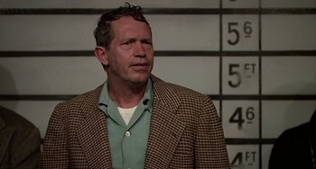 Movie still from “The Brink's Job” (1978), directed by William Friedkin – A man wearing a jacket standing in front of a wall; Close Up shot, Low angle