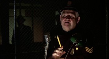 Movie still from “The Brink's Job” (1978), directed by William Friedkin – A man in a police uniform holding a pencil and a microphone; Close Up shot, Over the shoulder angle