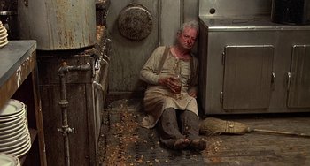 Movie still from “The Brink's Job” (1978), directed by William Friedkin – A man sitting on the ground holding a glass of water; Wide shot, Overhead angle