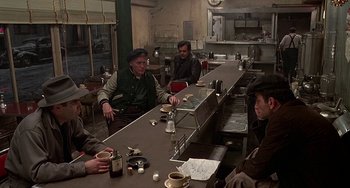 Movie still from “The Brink's Job” (1978), directed by William Friedkin – A group of men sitting at a long table in a restaurant; Wide shot, High angle