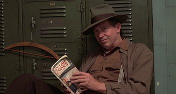 Movie still from “The Brink's Job” (1978), directed by William Friedkin – A man wearing a hat is holding a book; Medium shot, High angle