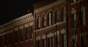 Movie still from “The Brink's Job” (1978), directed by William Friedkin – A man sitting on top of a building at night; Extreme Wide shot, Low angle