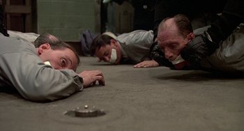 Movie still from “The Brink's Job” (1978), directed by William Friedkin – A group of men laying on the ground in a room; Wide shot, High angle