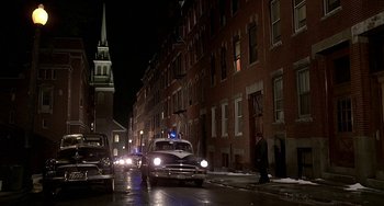 Movie still from “The Brink's Job” (1978), directed by William Friedkin – An old car driving down a street at night; Extreme Wide shot, High angle