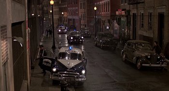Movie still from “The Brink's Job” (1978), directed by William Friedkin – A police car driving down a street at night; Extreme Wide shot, High angle