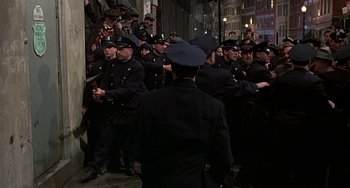 Movie still from “The Brink's Job” (1978), directed by William Friedkin – A group of men in police uniforms are standing in a crowd; Wide shot, High angle