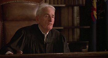 Movie still from “The Brink's Job” (1978), directed by William Friedkin – An older man in a black robe sitting in a courtroom; Close Up shot, Low angle