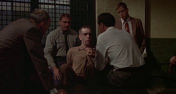 Movie still from “The Brink's Job” (1978), directed by William Friedkin – A group of men sitting around a man in a brown shirt; Medium shot, Over the shoulder angle