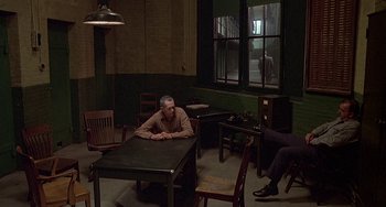 Movie still from “The Brink's Job” (1978), directed by William Friedkin – A man sitting at a table in front of another man; Wide shot, High angle