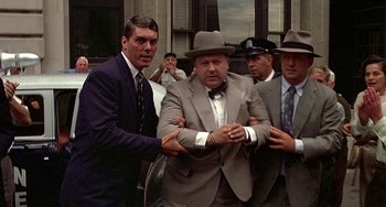 Movie still from “The Brink's Job” (1978), directed by William Friedkin – A group of men standing around each other in suits and hats; Wide shot, Over the shoulder angle