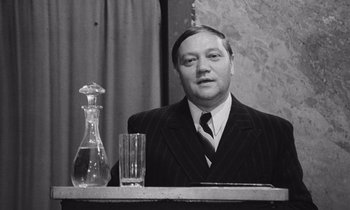 Movie still from “The Cremator” (1969), directed by Juraj Herz – A black and white photo of a man sitting at a table; Close Up shot, Over the shoulder angle