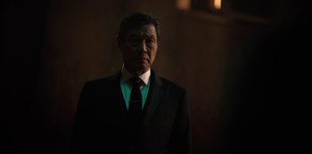 Movie still from “Altered Carbon” (2018), created by Laeta Kalogridis – A man in a suit and tie standing in a dark room; Medium shot, Low angle