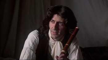 Movie still from “The Duellists” (1977), directed by Ridley Scott – A man with long black hair holding a wooden stick; Close Up shot, Low angle