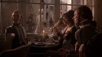 Movie still from “The Duellists” (1977), directed by Ridley Scott – A group of people sitting around a table with food; Medium shot, Over the shoulder angle