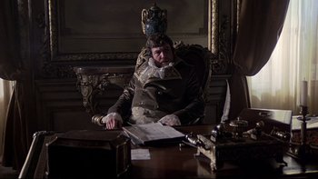 Movie still from “The Duellists” (1977), directed by Ridley Scott – A man sitting at a table in a room; Medium shot, Low angle