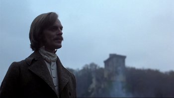 Movie still from “The Duellists” (1977), directed by Ridley Scott – A man with a long hair and a beard standing in front of a castle; Medium shot, Low angle