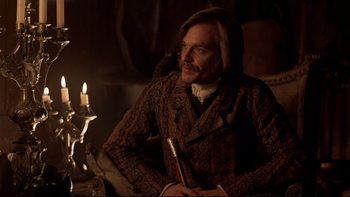 Movie still from “The Duellists” (1977), directed by Ridley Scott – A man sitting in front of a lit candle in a room; Medium shot, Over the shoulder angle