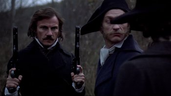 Movie still from “The Duellists” (1977), directed by Ridley Scott – Two men are holding guns in a forest; Medium shot, Over the shoulder angle