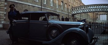 Movie still from “The Eagle Has Landed” (1976), directed by John Sturges – An old car parked in front of a brick building; Wide shot, Low angle