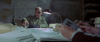 Movie still from “The Eagle Has Landed” (1976), directed by John Sturges – A man in a uniform sitting at a table with papers; Medium shot, Over the shoulder angle