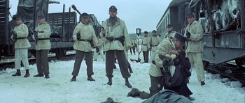Movie still from “The Eagle Has Landed” (1976), directed by John Sturges – A group of men standing next to a train in the snow; Wide shot, Over the shoulder angle