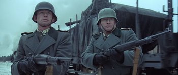 Movie still from “The Eagle Has Landed” (1976), directed by John Sturges – Two men in military uniforms are standing next to each other holding guns; Medium shot, Low angle