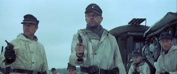 Movie still from “The Eagle Has Landed” (1976), directed by John Sturges – A man holding a gun while standing in front of other men; Medium shot, Low angle