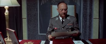 Movie still from “The Eagle Has Landed” (1976), directed by John Sturges – A man sitting in a chair reading a document; Medium shot, Low angle