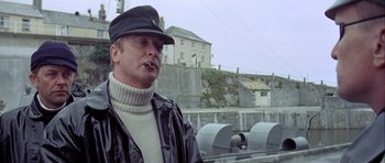 Movie still from “The Eagle Has Landed” (1976), directed by John Sturges – A man wearing a leather jacket and hat smoking a cigarette; Medium shot, Low angle