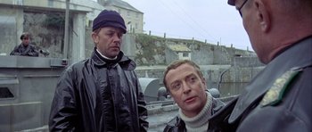 Movie still from “The Eagle Has Landed” (1976), directed by John Sturges – Two men standing next to each other on a bridge; Medium shot, Low angle