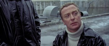 Movie still from “The Eagle Has Landed” (1976), directed by John Sturges – A man in a black jacket and a white sweater; Close Up shot, Over the shoulder angle