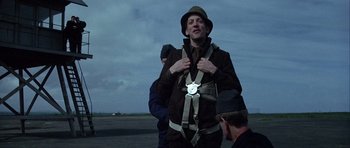 Movie still from “The Eagle Has Landed” (1976), directed by John Sturges – A man wearing a hat and a harness on a runway; Medium shot, Low angle