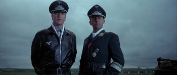 Movie still from “The Eagle Has Landed” (1976), directed by John Sturges – A couple of men standing next to each other in uniforms; Medium shot, Low angle