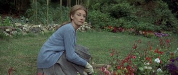 Movie still from “The Eagle Has Landed” (1976), directed by John Sturges – A woman kneeling down in the grass near some flowers; Medium shot, Over the shoulder angle