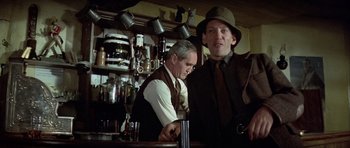 Movie still from “The Eagle Has Landed” (1976), directed by John Sturges – A man in a suit and hat standing at a bar; Medium shot, Low angle