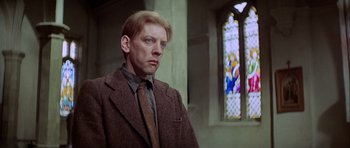 Movie still from “The Eagle Has Landed” (1976), directed by John Sturges – A man wearing a suit and tie standing in front of a stained glass window; Close Up shot, Low angle