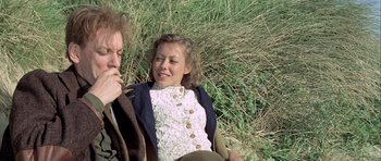 Movie still from “The Eagle Has Landed” (1976), directed by John Sturges – A woman sitting next to a man in a field; Medium shot, Over the shoulder angle