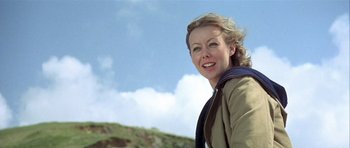 Movie still from “The Eagle Has Landed” (1976), directed by John Sturges – A woman standing on top of a hill with clouds in the background; Close Up shot, Low angle