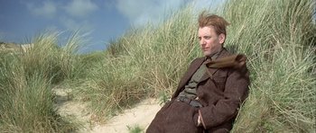 Movie still from “The Eagle Has Landed” (1976), directed by John Sturges – A man sitting on the ground in a field; Medium shot, Low angle