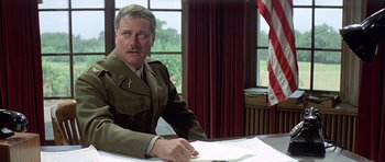 Movie still from “The Eagle Has Landed” (1976), directed by John Sturges – A man in a military uniform sitting at a table; Medium shot, Over the shoulder angle