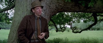 Movie still from “The Eagle Has Landed” (1976), directed by John Sturges – A man smoking a cigarette while standing next to a tree; Medium shot, Low angle