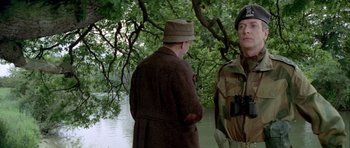 Movie still from “The Eagle Has Landed” (1976), directed by John Sturges – Two men standing next to each other near a body of water; Medium shot, Over the shoulder angle