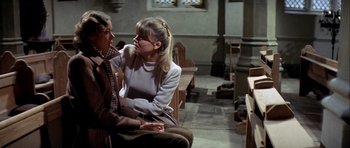 Movie still from “The Eagle Has Landed” (1976), directed by John Sturges – Two women sitting in a church with a stained glass window in the background; Medium shot, Over the shoulder angle