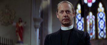 Movie still from “The Eagle Has Landed” (1976), directed by John Sturges – A man wearing a priest's outfit in a room; Close Up shot, Low angle