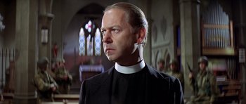 Movie still from “The Eagle Has Landed” (1976), directed by John Sturges – A man wearing a priest's outfit in front of stained glass windows; Close Up shot, Low angle