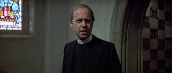 Movie still from “The Eagle Has Landed” (1976), directed by John Sturges – A man wearing a priest's outfit standing in front of a wall; Close Up shot, Low angle