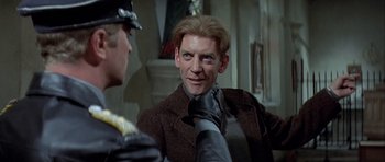 Movie still from “The Eagle Has Landed” (1976), directed by John Sturges – A man in a brown coat and a black hat; Close Up shot, Over the shoulder angle