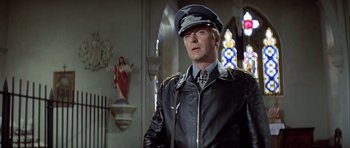 Movie still from “The Eagle Has Landed” (1976), directed by John Sturges – A man in a leather jacket wearing a hat and tie; Medium shot, Low angle