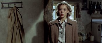 Movie still from “The Eagle Has Landed” (1976), directed by John Sturges – A woman wearing a brown coat standing next to a wooden pole; Close Up shot, Low angle